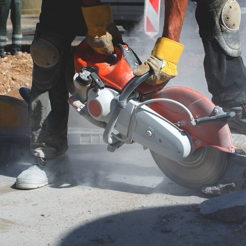 Builder worker with cut-off machine power tool breaking concrete at road construction site